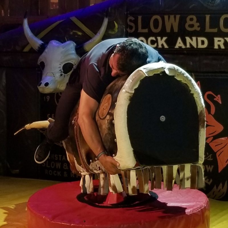 Corporate Pub Crawl Guest Riding A Mechanical Bull Backwards And Hanging On For Dear Life.